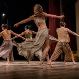 Patru dansatori sunt pe o scenă de teatru, surprinși în mișcare în timpul unui spectacol